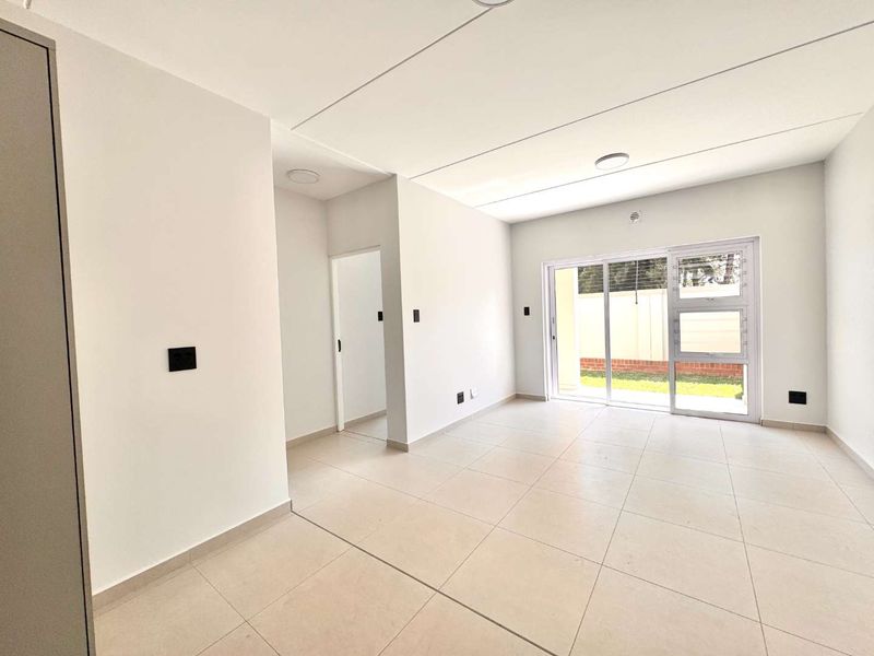 A bright, modern, and empty living area featuring neutral tiled flooring and a large sliding glass door providing access to the exterior.