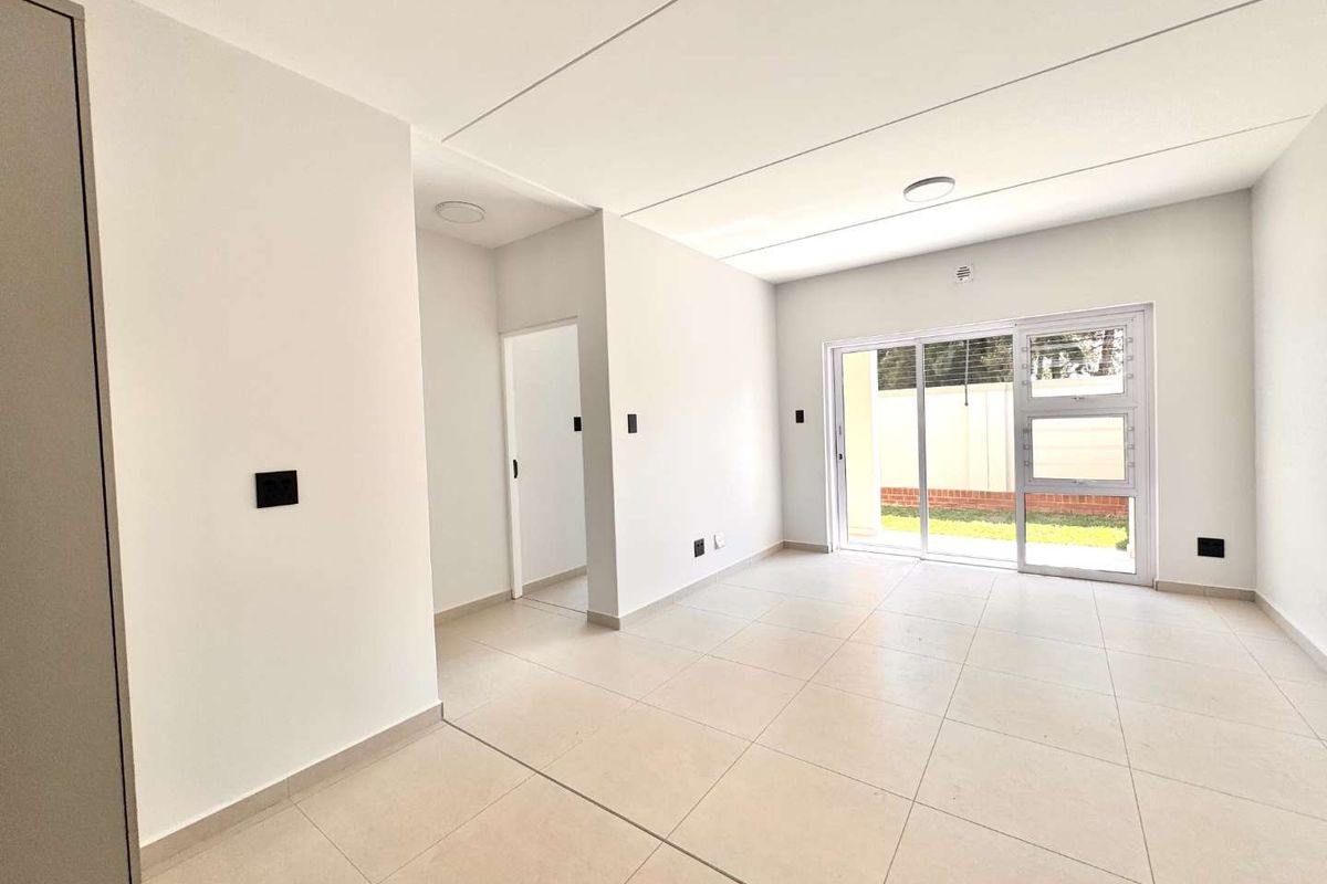 A bright, modern, and empty living area featuring neutral tiled flooring and a large sliding glass door providing access to the exterior.
