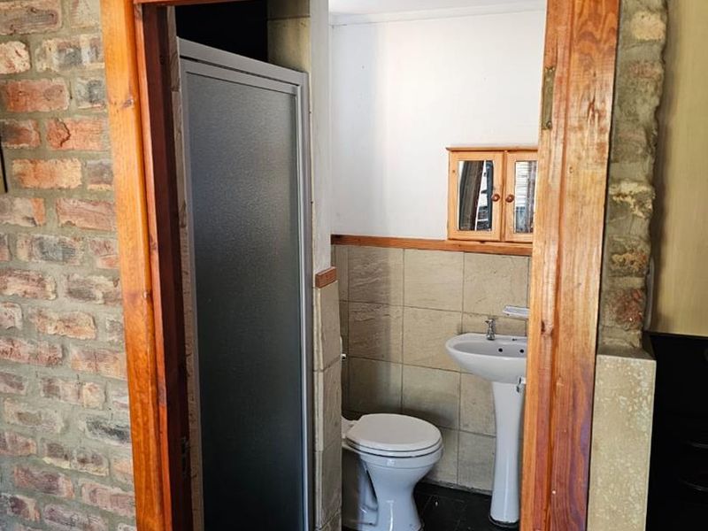 A compact bathroom featuring a pedestal basin, toilet, and shower enclosure, finished with tiled flooring and exposed brick wall accents.