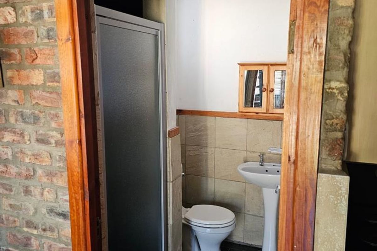 A compact bathroom featuring a pedestal basin, toilet, and shower enclosure, finished with tiled flooring and exposed brick wall accents.