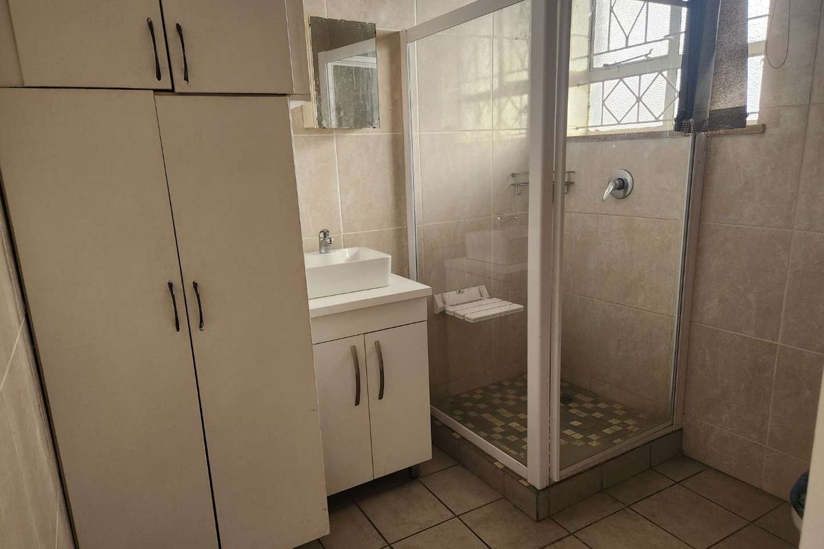 A functional bathroom featuring a shower enclosure, vanity with vessel sink, and built-in storage cabinetry, finished with neutral wall and floor tiles.