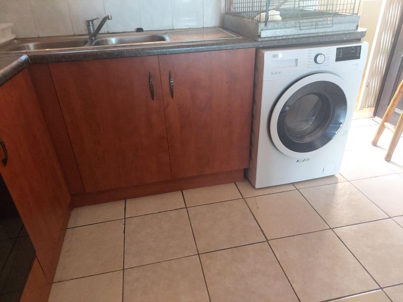 A functional laundry area featuring laminate cabinetry, a stainless steel sink, tiled splashback, and ceramic floor tiles.