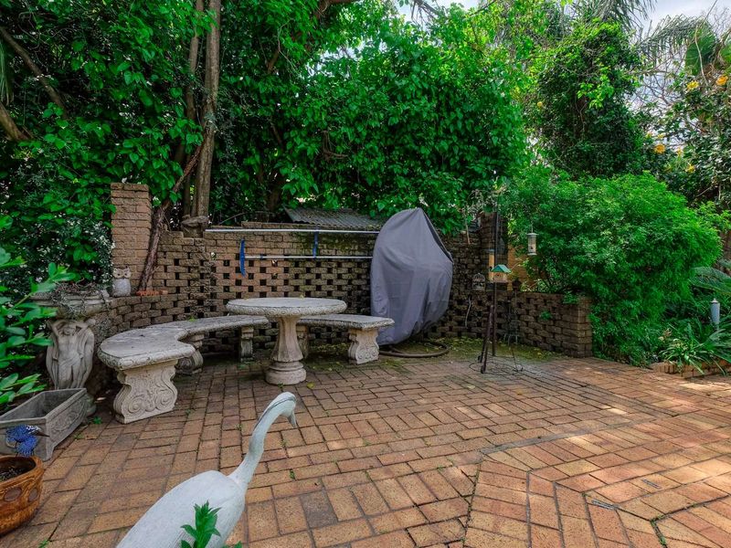 A private outdoor patio area featuring brick paving and a built-in stone table and bench set, surrounded by mature garden greenery.