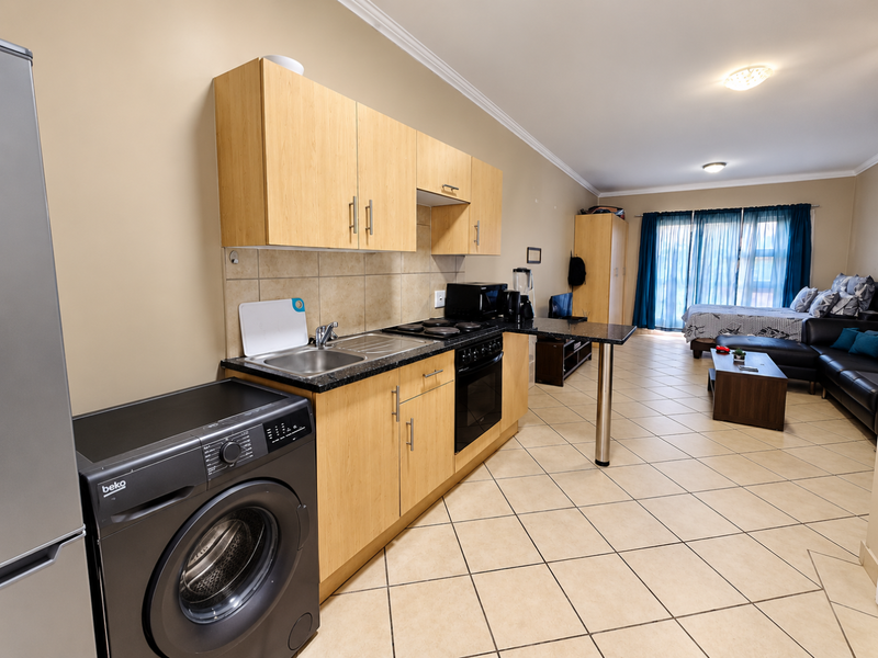 Open-plan apartment living area featuring a compact kitchen with light wood cabinetry, integrated appliances, and a breakfast bar flowing into the bedroom space.