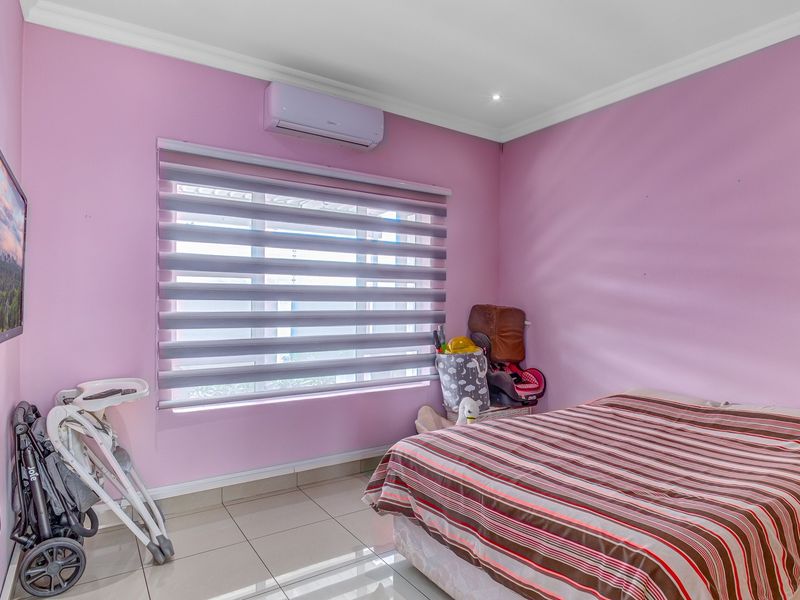 A bedroom featuring tiled flooring, a wall-mounted split-system air conditioner, and modern zebra blinds.