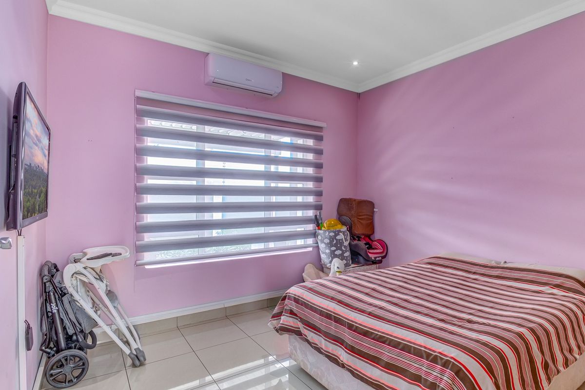 A bedroom featuring tiled flooring, a wall-mounted split-system air conditioner, and modern zebra blinds.