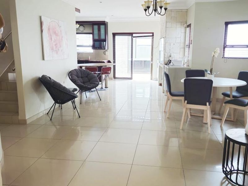 Spacious open-plan living and dining area featuring large format floor tiles, a stone-clad feature wall, and direct access to an outdoor patio.