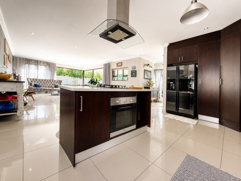 Modern open-plan kitchen and living area featuring a central island with built-in oven, gas hob, extractor fan, and sleek dark wood cabinetry.