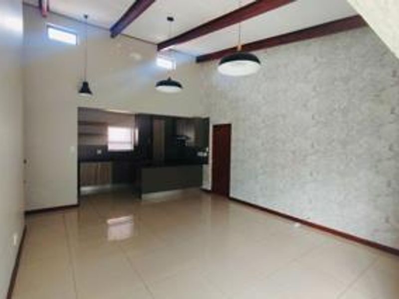 Spacious open-plan living area featuring high ceilings with exposed timber beams, tiled flooring, and a modern kitchen with built-in cabinetry.