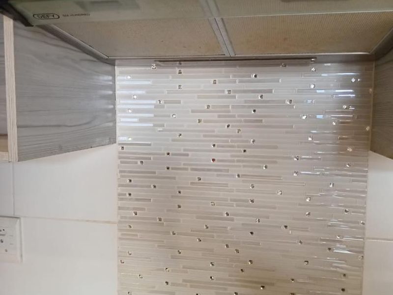 A close-up view of a kitchen workspace featuring a stainless steel extractor fan, a decorative mosaic tile backsplash, and a built-in electric cooktop.