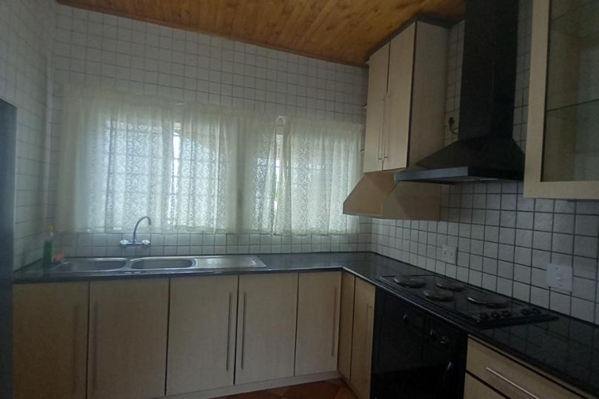 A functional kitchen featuring built-in cabinetry, a dark countertop, integrated oven and hob, extractor fan, and a double sink with tiled splashbacks.