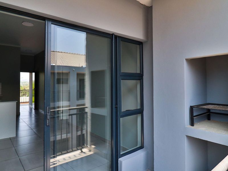 A modern balcony featuring a built-in braai, tiled flooring, and a sliding glass door providing access to the interior living space.