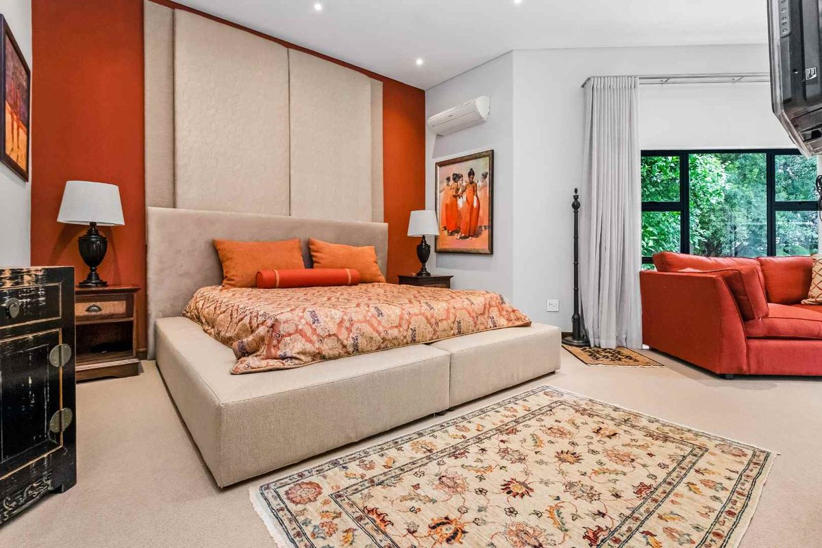 Spacious bedroom featuring a large upholstered headboard, recessed ceiling lighting, and a wall-mounted air conditioning unit with large windows overlooking greenery.