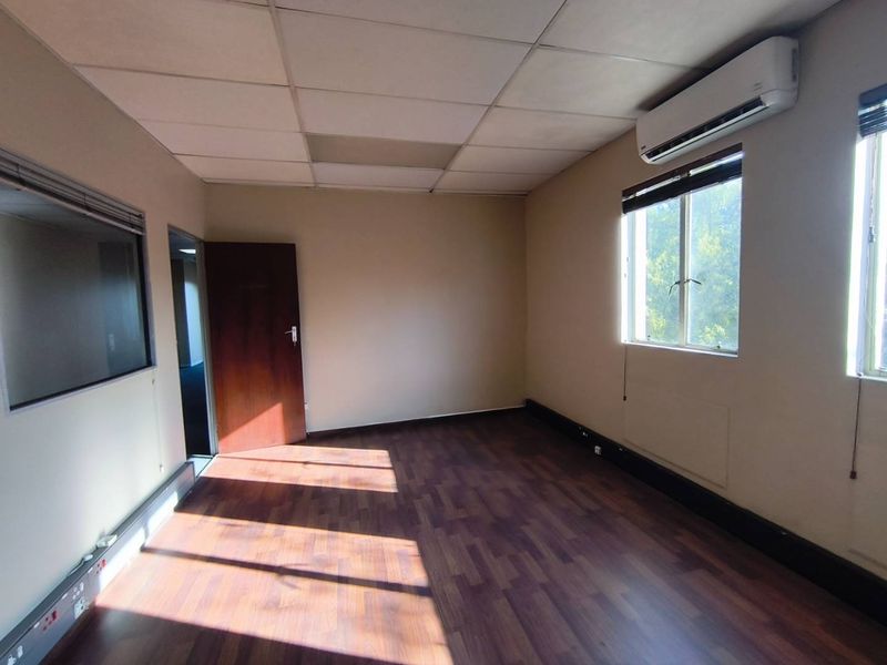 A vacant office space featuring laminate flooring, a suspended ceiling, integrated air conditioning, and an internal glass partition wall.