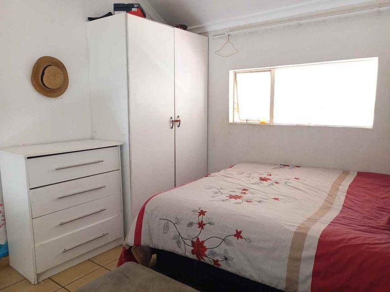 A compact bedroom featuring tiled flooring, a built-in wardrobe, and a window providing natural light.