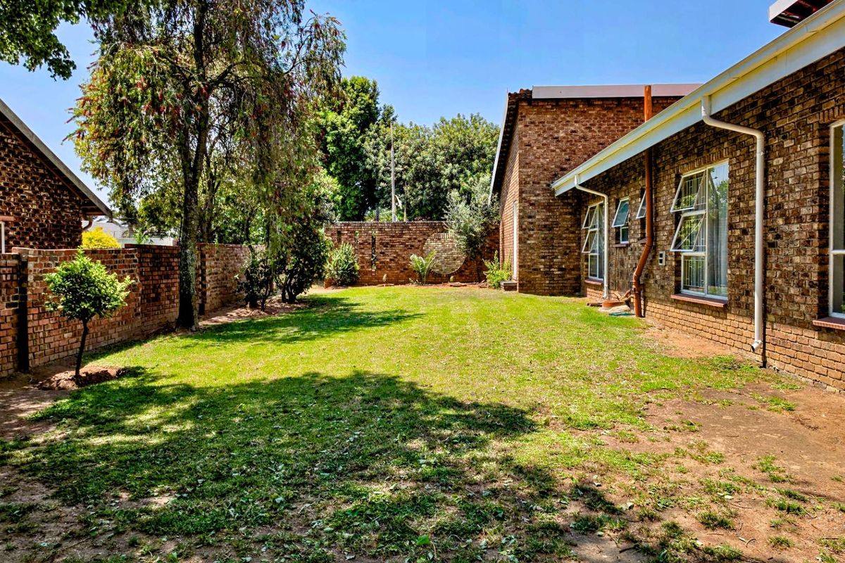 A spacious rear garden featuring established lawn, brick boundary walls, and a face brick house exterior with aluminium window frames.