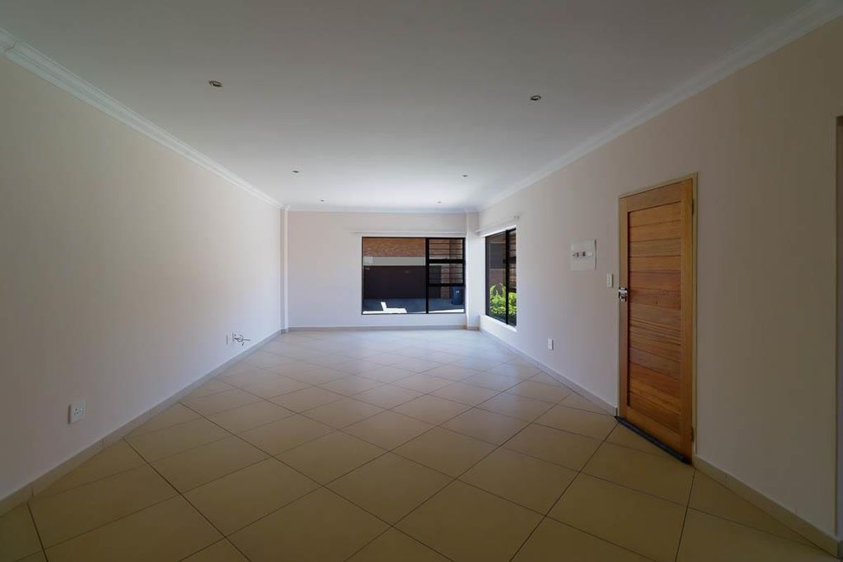 A spacious, empty living area featuring neutral tiled flooring, recessed downlighting, and a solid timber door, offering a clean canvas for interior design.