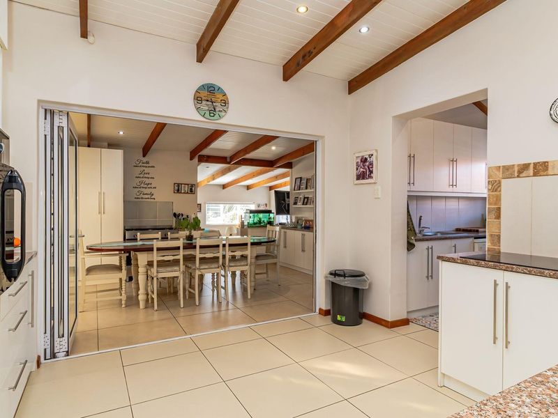 Spacious open-plan kitchen and dining area featuring exposed timber beams, tiled flooring, granite countertops, and seamless flow through bi-fold doors to the adjacent space.