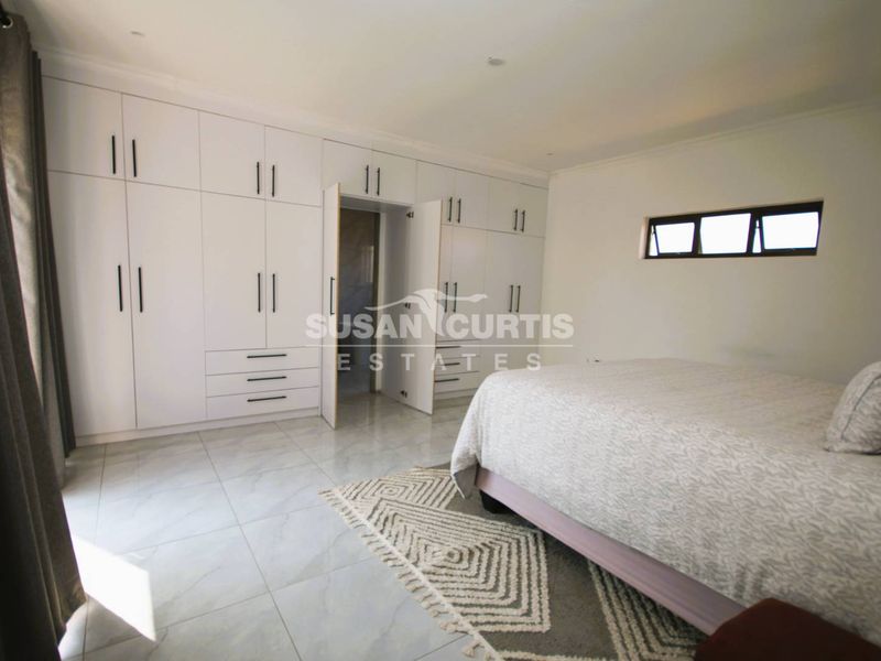 Spacious bedroom featuring extensive white built-in cupboards, modern tiled flooring, and a horizontal window providing natural light.