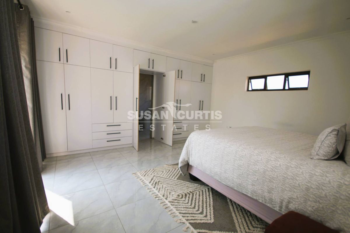Spacious bedroom featuring extensive white built-in cupboards, modern tiled flooring, and a horizontal window providing natural light.