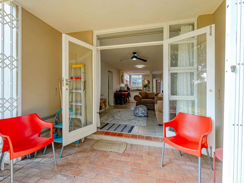 Covered patio area with brick flooring and security gate, providing direct access to the open-plan living and kitchen space through double french doors.