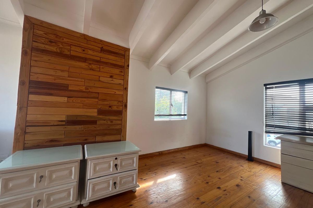 Spacious bedroom featuring exposed timber ceiling beams, hardwood flooring, and a decorative timber feature wall with natural light from multiple windows.