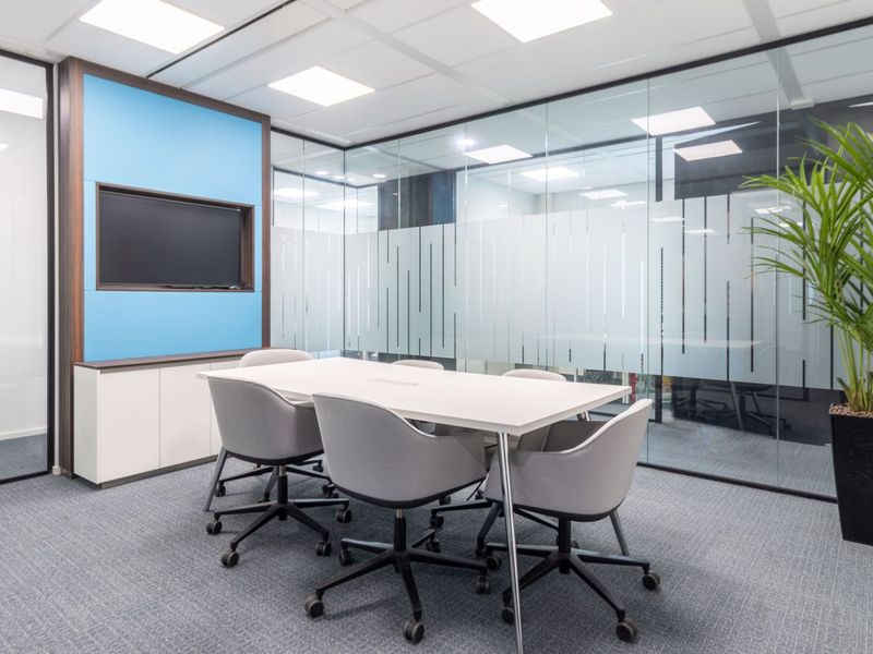 Modern professional meeting room featuring glass partition walls, recessed ceiling lighting, built-in cabinetry, and high-quality carpet flooring.