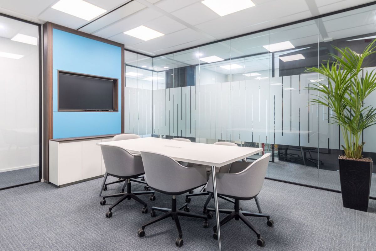 Modern professional meeting room featuring glass partition walls, recessed ceiling lighting, built-in cabinetry, and high-quality carpet flooring.