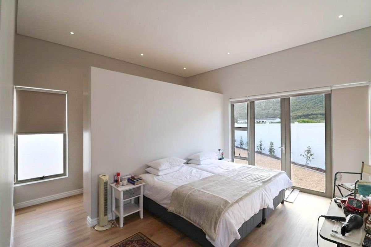 A bright, modern bedroom featuring light timber flooring, recessed ceiling lighting, and large glass sliding doors providing direct access to the outdoor area.