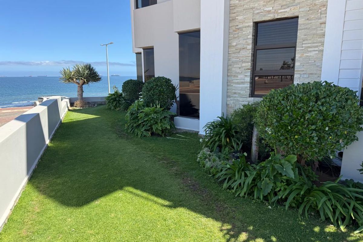 A well-maintained rear garden area featuring stone-clad exterior walls, manicured lawn, and established landscaping with direct ocean views.