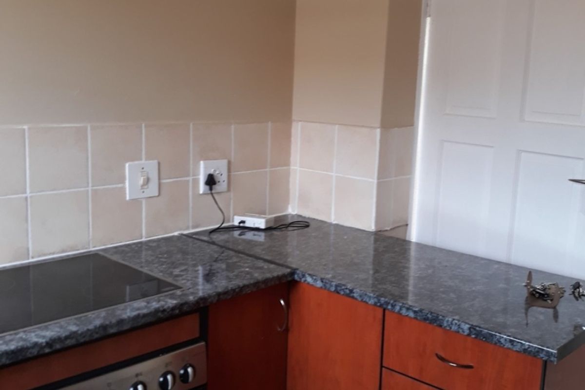 A functional kitchen area featuring built-in cabinetry, a ceramic hob, oven, and durable laminate countertops with a neutral tiled backsplash.
