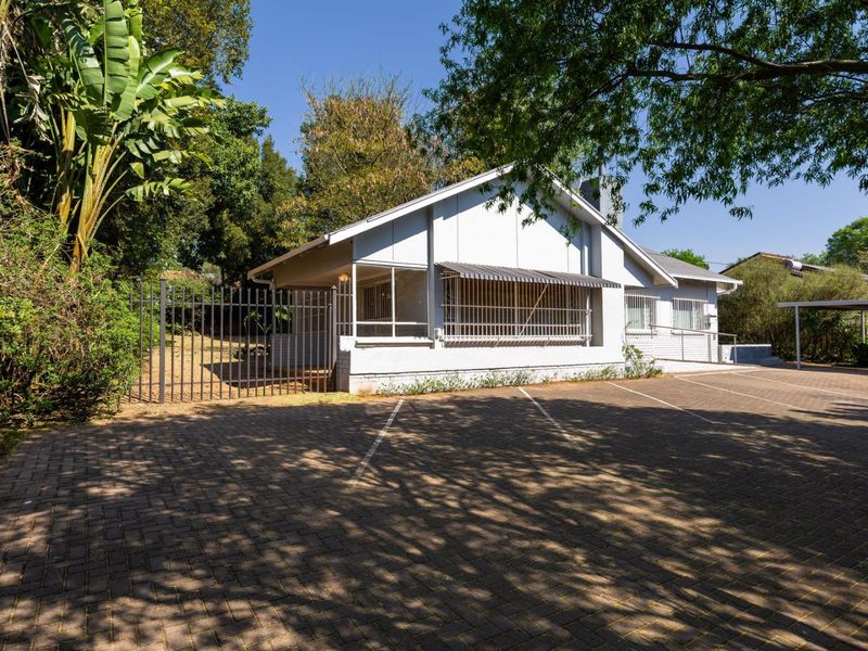 Front exterior view of the property featuring a paved driveway, metal security fencing, and a carport area.