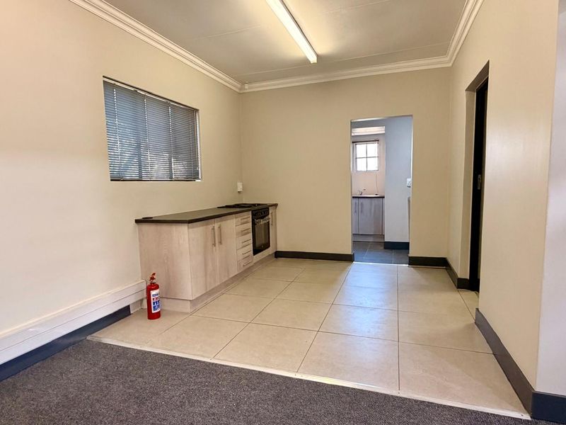A functional kitchen area featuring built-in cabinetry, an integrated oven and hob, tiled flooring, and a view through to an adjacent utility space.