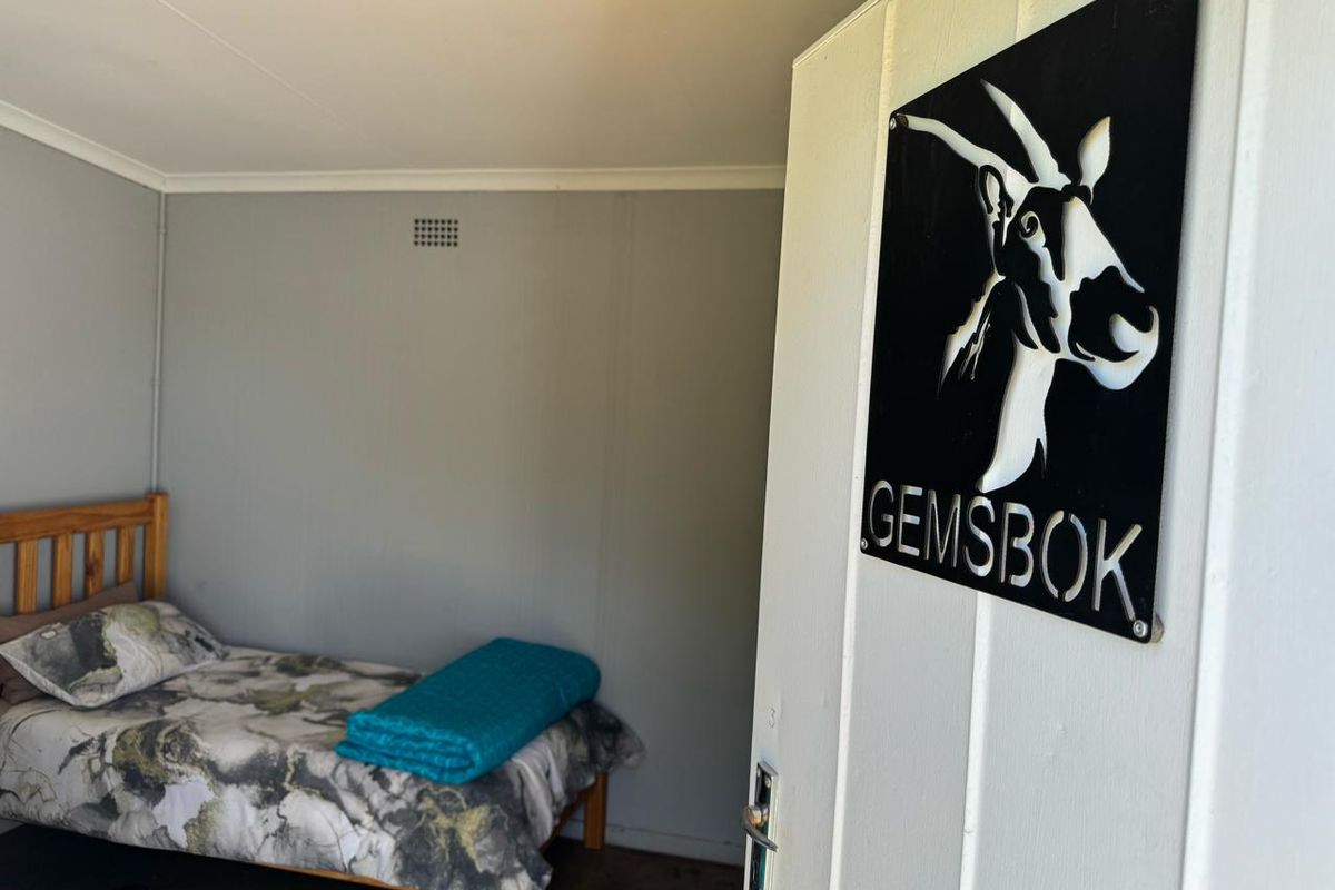 A bedroom interior featuring neutral wall finishes, a ventilation grille, and a door with a decorative metal sign.