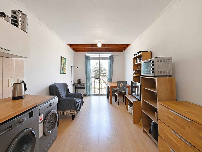 Open-plan living area featuring laminate flooring, exposed timber ceiling beams, and direct access to a balcony through sliding glass doors.