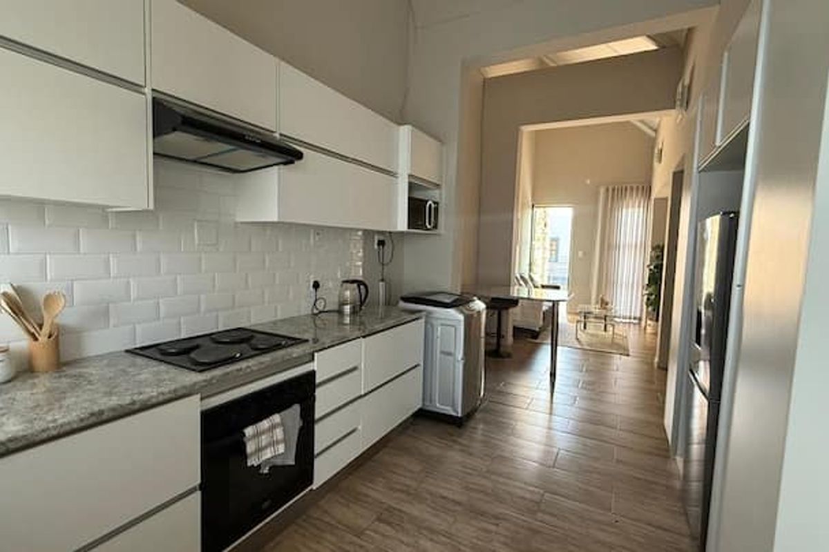 Modern kitchen featuring white handleless cabinetry, subway tile backsplash, stone-look countertops, and integrated appliances, flowing into an open-plan living area.