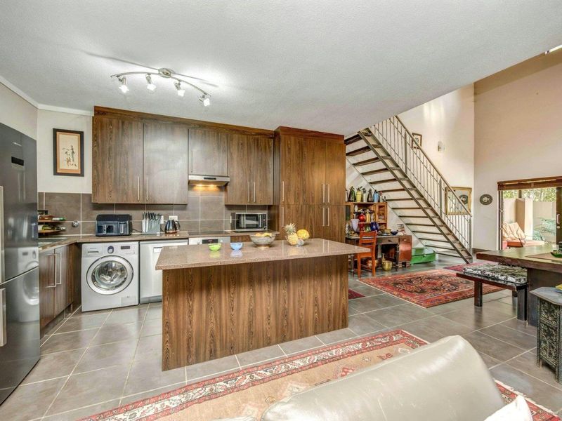 Open-plan kitchen and living area featuring dark wood cabinetry, a stone island, tiled floors, and a staircase leading to the upper level.