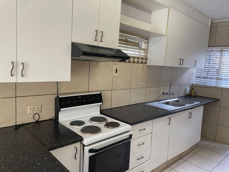 A functional kitchen featuring white cabinetry, dark laminate countertops, a double bowl sink, and a built-in electric stove with an extractor fan.