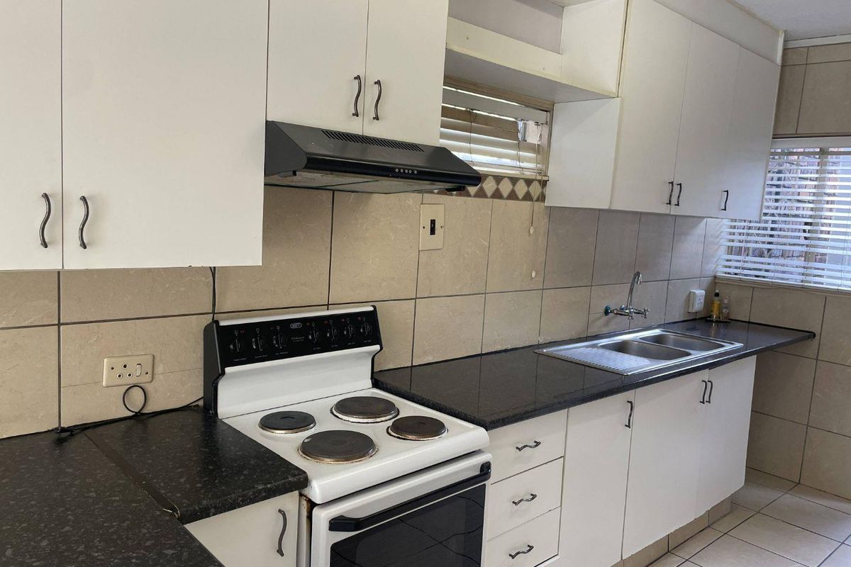 A functional kitchen featuring white cabinetry, dark laminate countertops, a double bowl sink, and a built-in electric stove with an extractor fan.