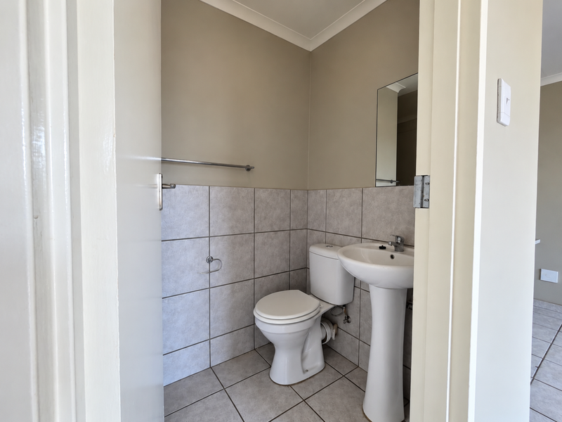 A clean and functional guest bathroom featuring a pedestal washbasin, toilet, and neutral tiled finishes.