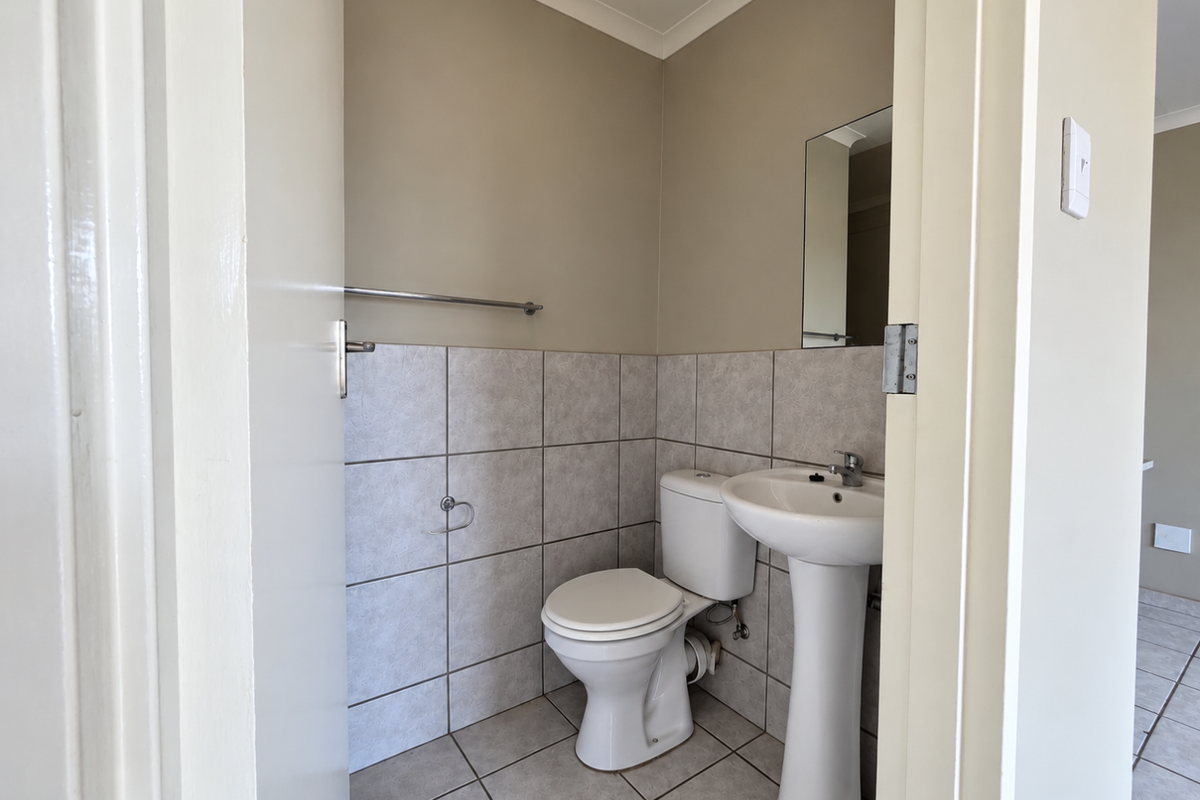 A clean and functional guest bathroom featuring a pedestal washbasin, toilet, and neutral tiled finishes.