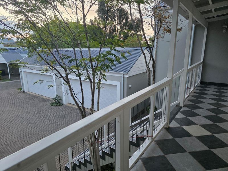 A covered balcony featuring checkered tile flooring and white timber railings, overlooking a paved driveway and garage area.
