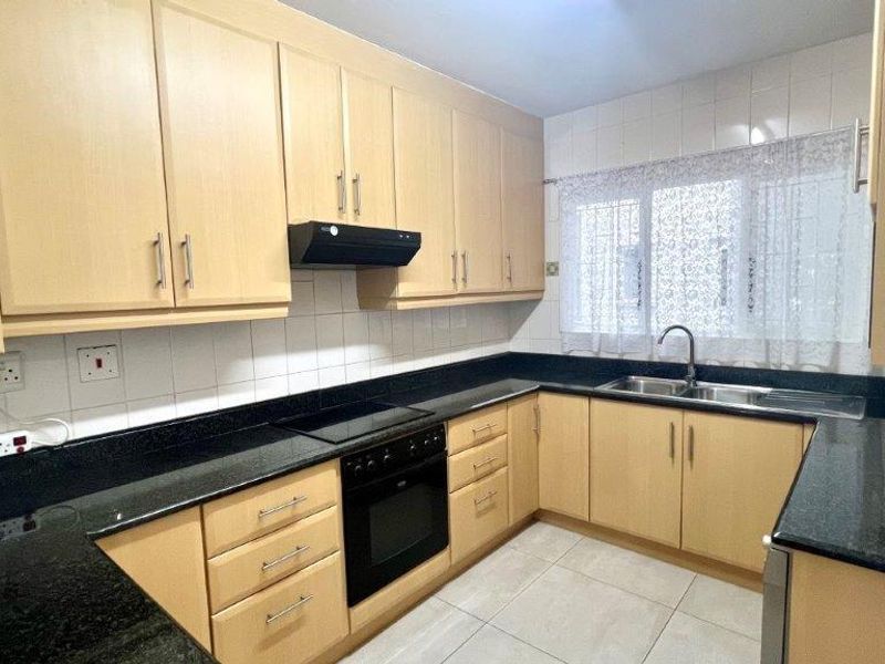 A functional kitchen featuring light wood cabinetry, black granite countertops, integrated oven and hob, and tiled finishes throughout.
