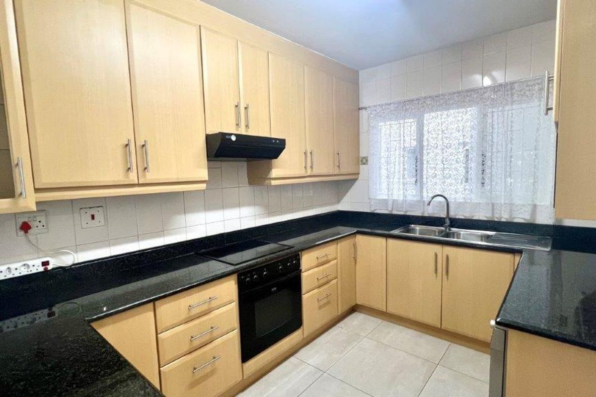 A functional kitchen featuring light wood cabinetry, black granite countertops, integrated oven and hob, and tiled finishes throughout.