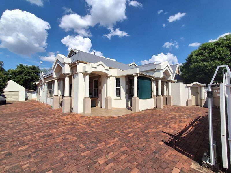 Front exterior view of a property featuring a brick paved driveway, covered porch with decorative columns, and a pitched roof design.