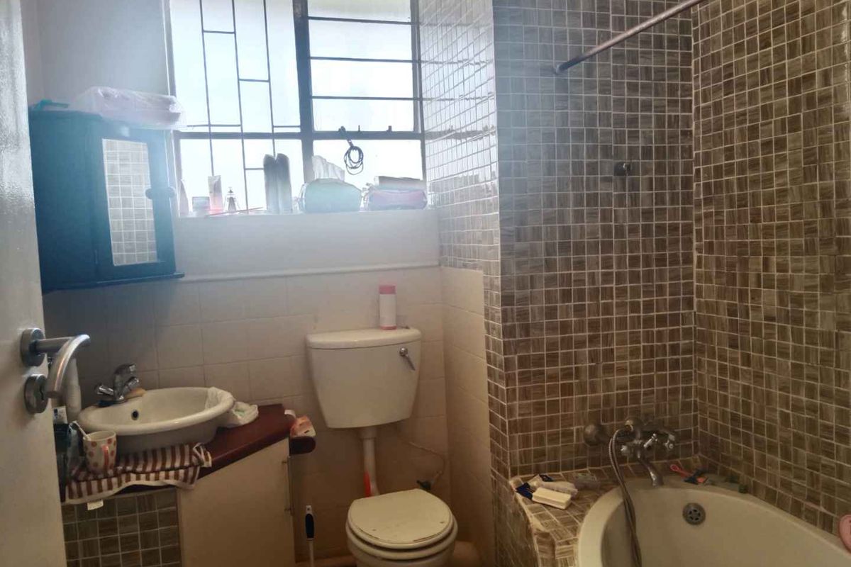 A compact bathroom featuring a built-in bathtub with mosaic tiling, a corner vanity unit, and a standard toilet, requiring cosmetic updates.