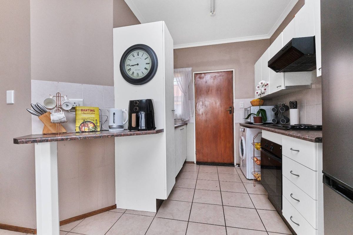 A functional kitchen featuring white cabinetry, a built-in oven, extractor fan, and tiled flooring, with a breakfast bar area and direct exterior access.