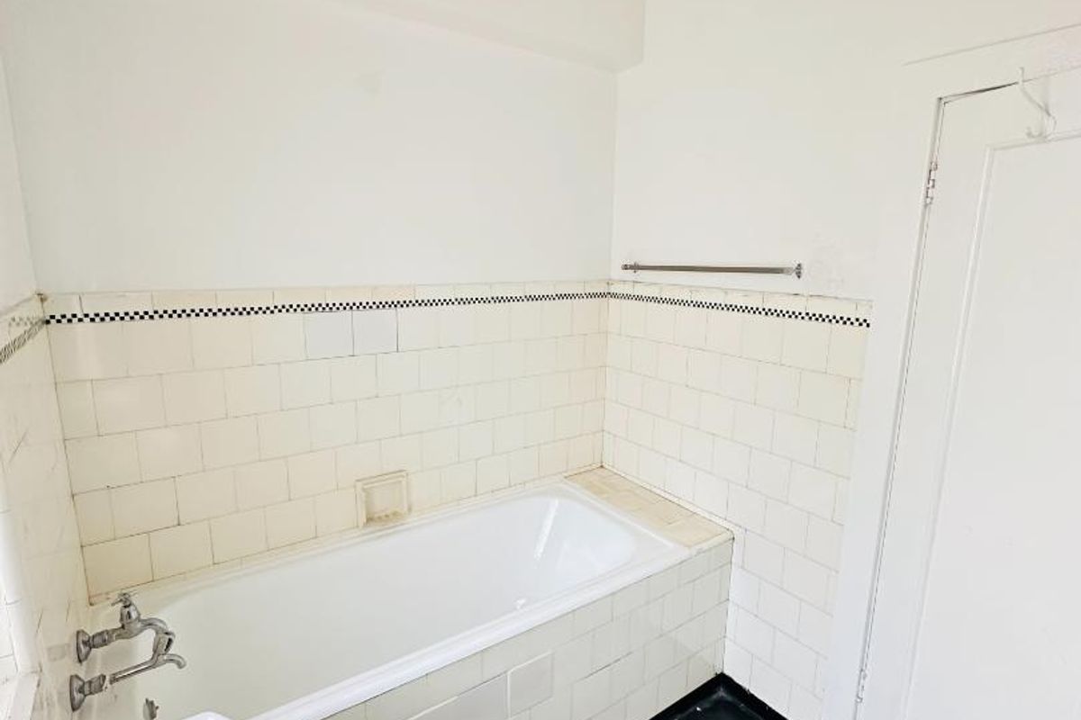 A functional bathroom featuring a built-in bathtub, pedestal basin, and classic tiled splashback, offering a blank canvas for modern renovation.