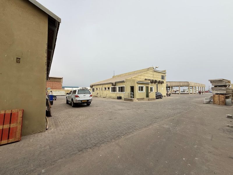 Exterior view of an industrial property featuring a paved yard, main building with external air conditioning units, and a covered loading structure.