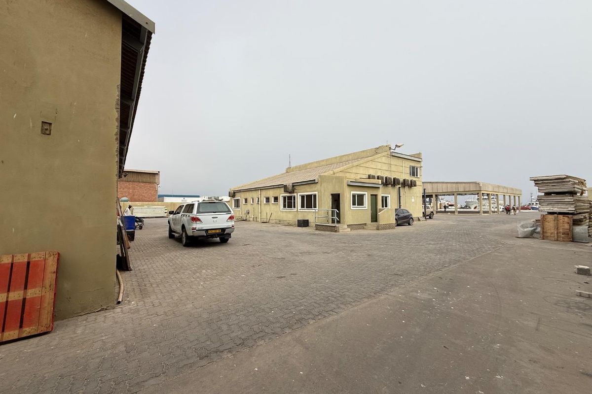 Exterior view of an industrial property featuring a paved yard, main building with external air conditioning units, and a covered loading structure.